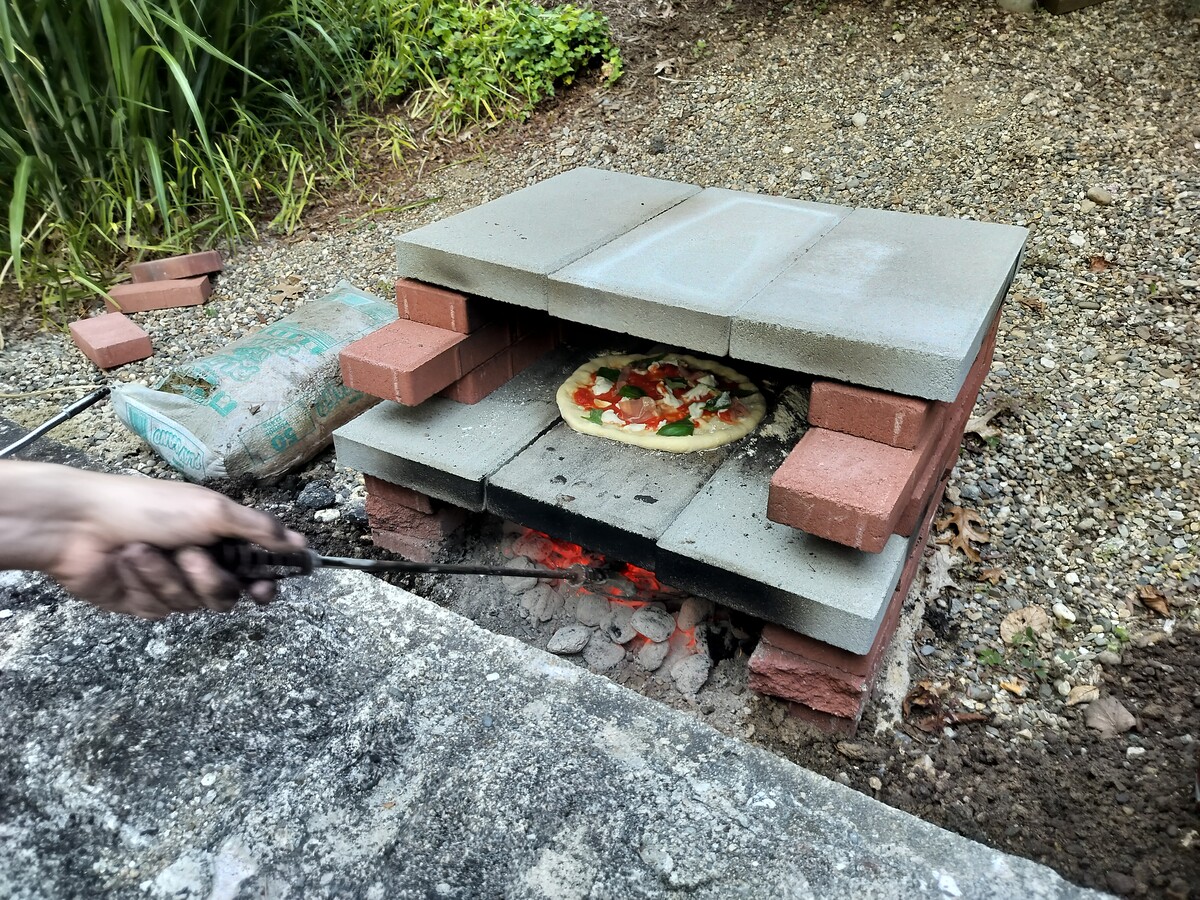Pizza oven in use, pizza cooking, and charcoal being stoked